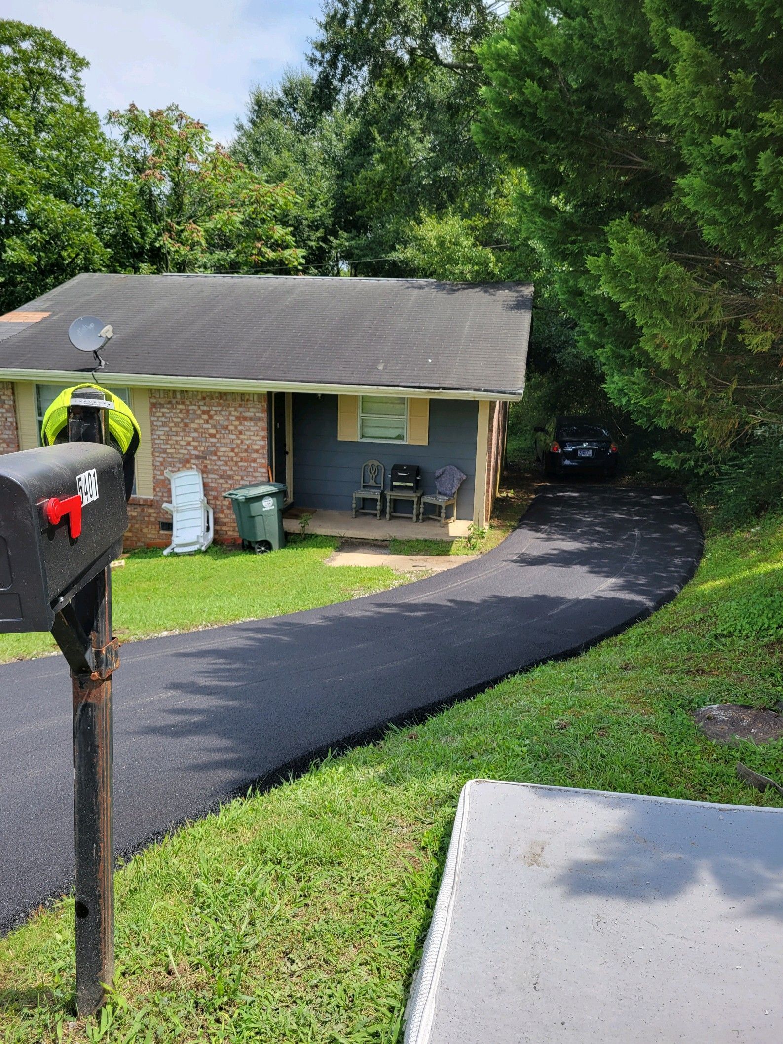 Black asphalt driveway leads to a small house with a blue exterior and mailbox on the left.