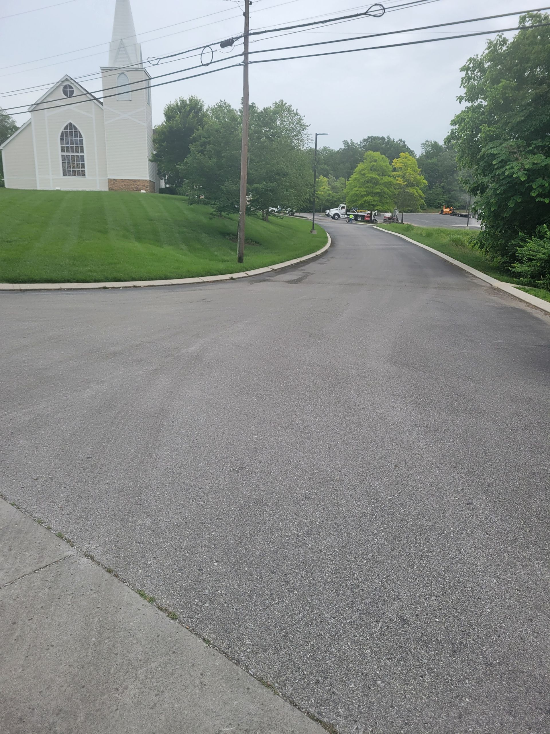 Road leading to a white church with a steeple on a grassy hill; overcast sky.