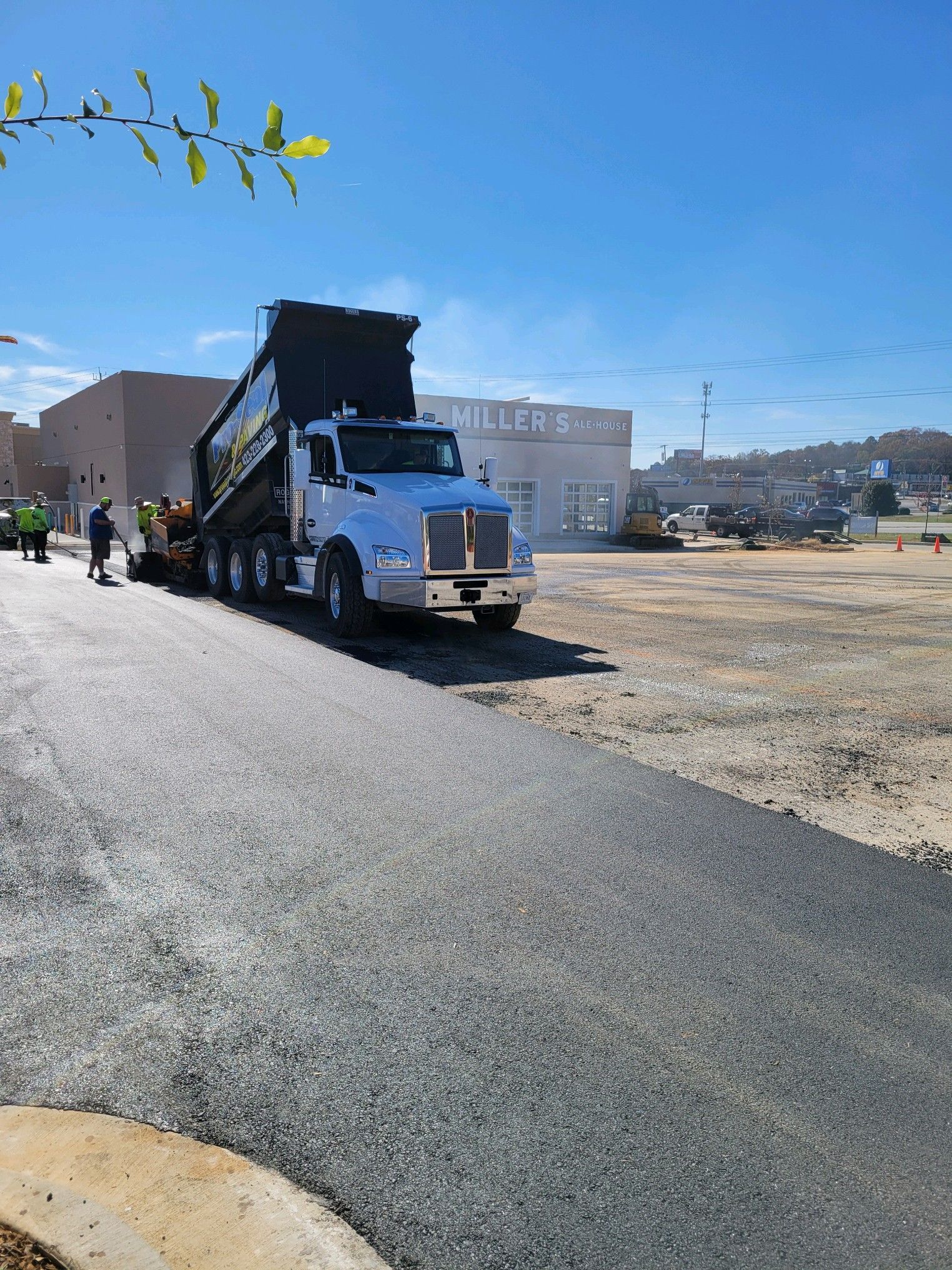 Asphalt paving project: Dump truck unloading asphalt onto a new road surface on a sunny day.