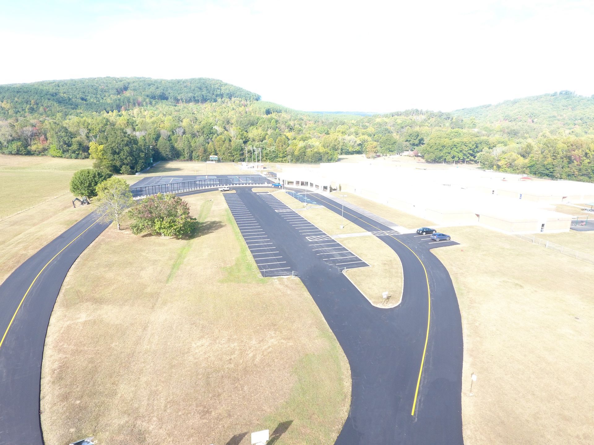 Aerial view of an airfield with paved runways, surrounded by grassy fields and forested hills.