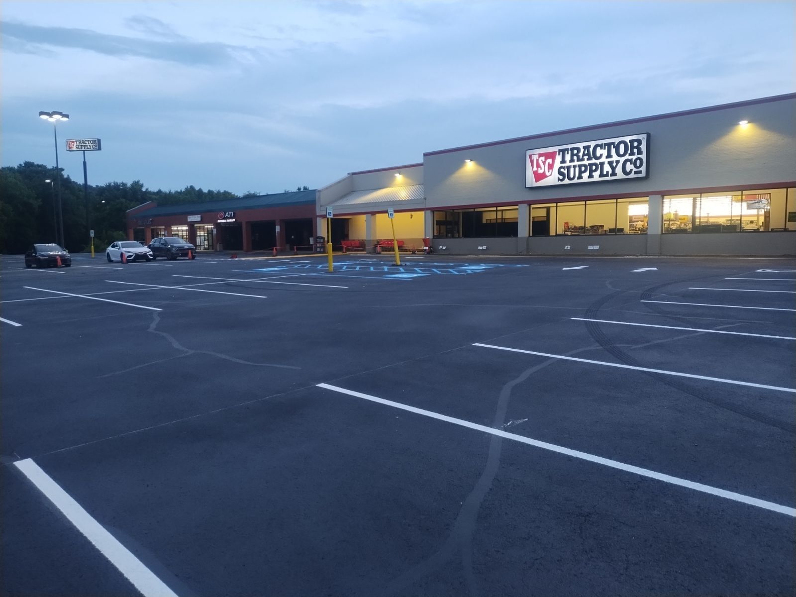 Tractor Supply Co. store exterior with empty parking lot; gray asphalt, white parking lines, dusk setting.