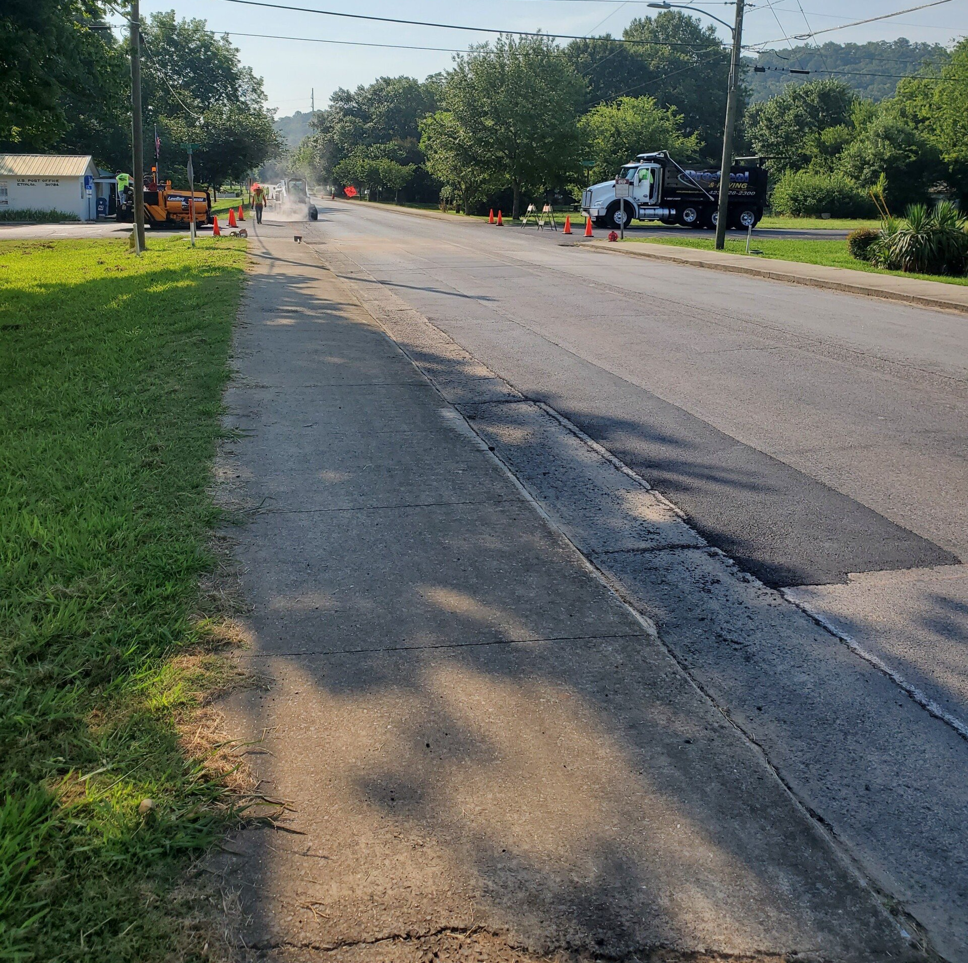 Road construction scene: paving work on a street with cones, trucks, and equipment visible.