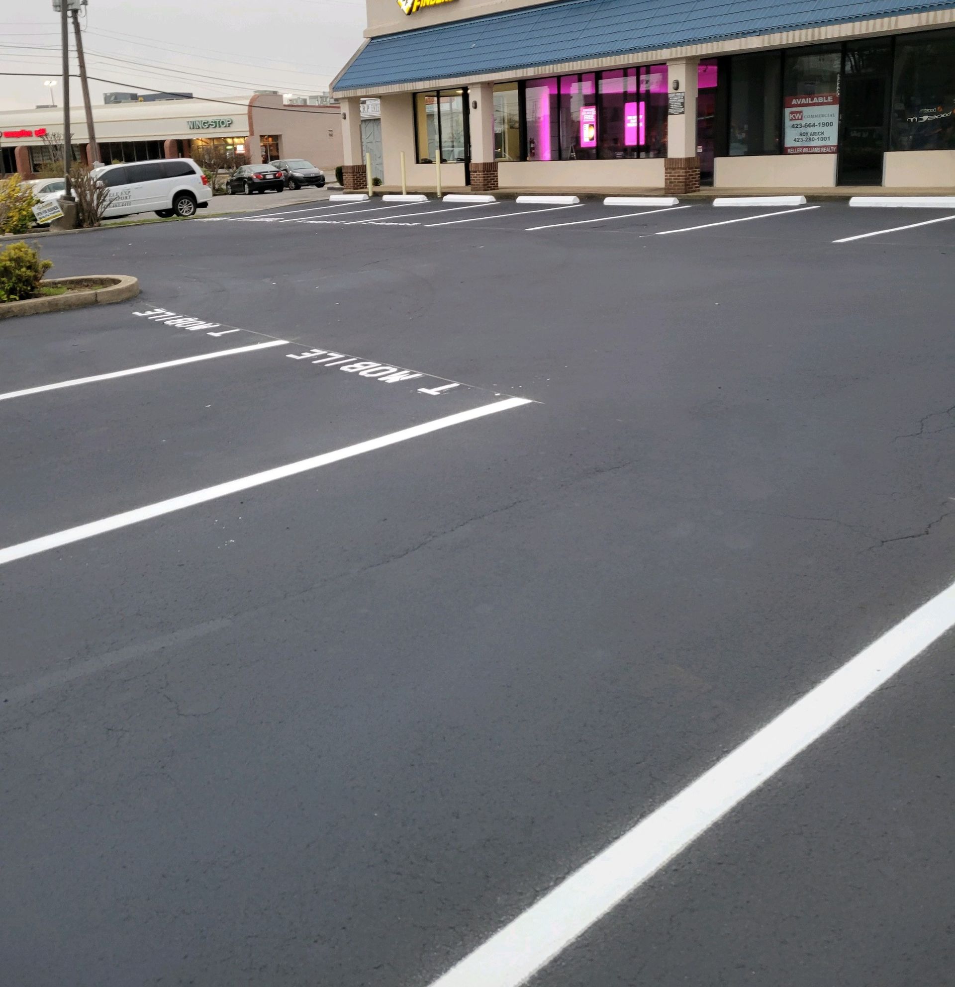 Newly paved, dark asphalt parking lot with white painted parking space lines in front of a storefront.
