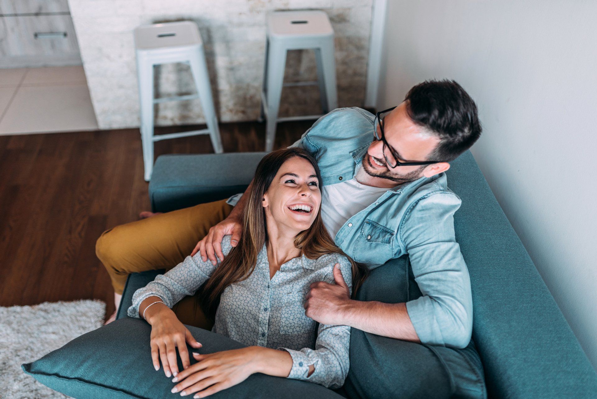 A man and a woman are laying on a couch in a living room.