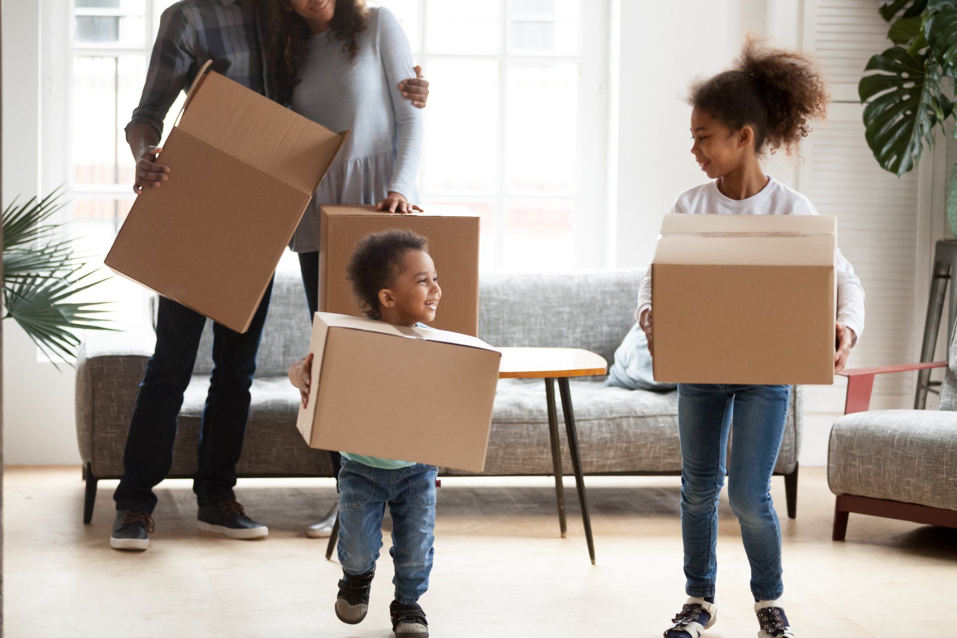 A family is holding cardboard boxes in a living room.