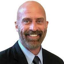 A bald man with a beard is wearing a suit and tie and smiling.