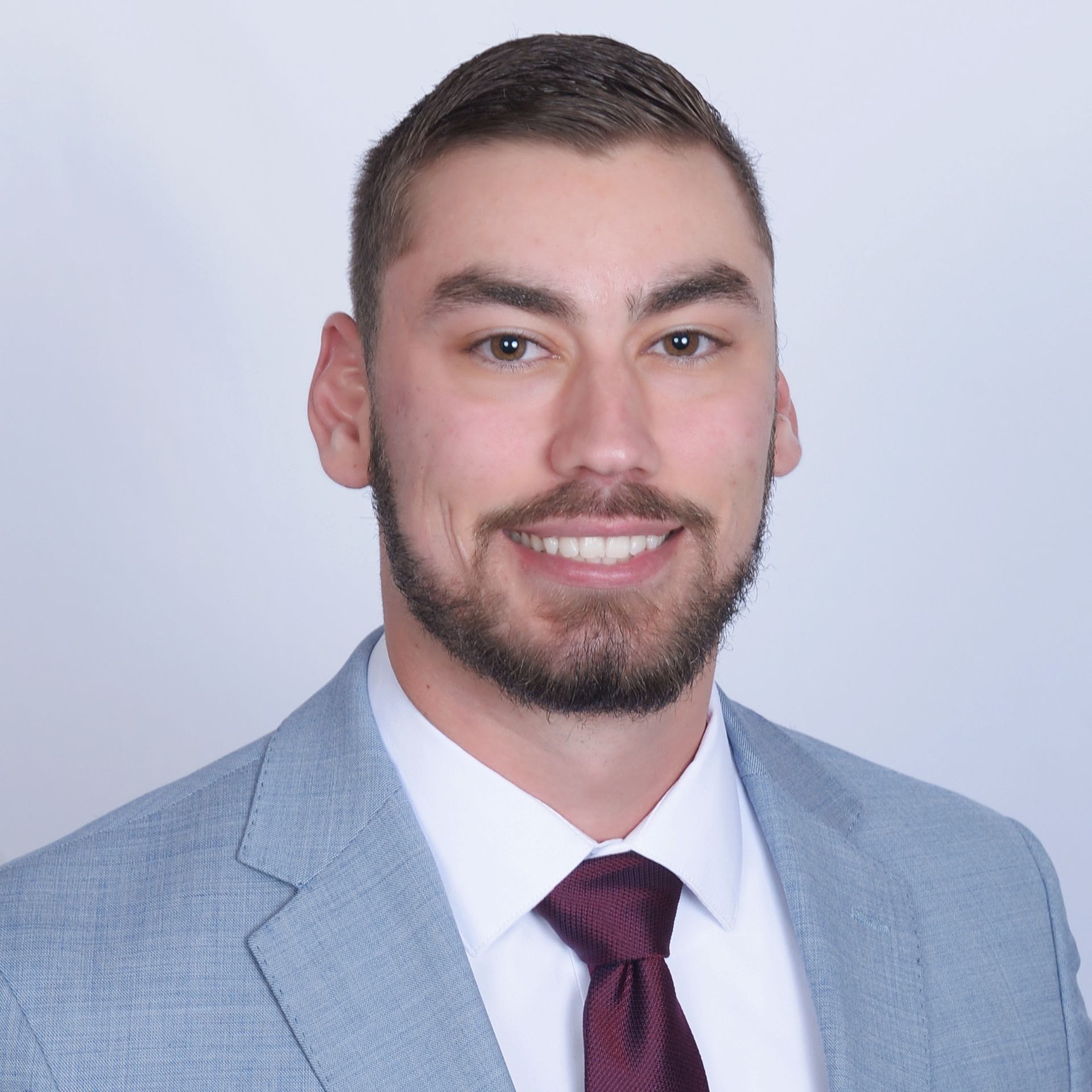 A man with a beard is wearing a suit and tie and smiling.