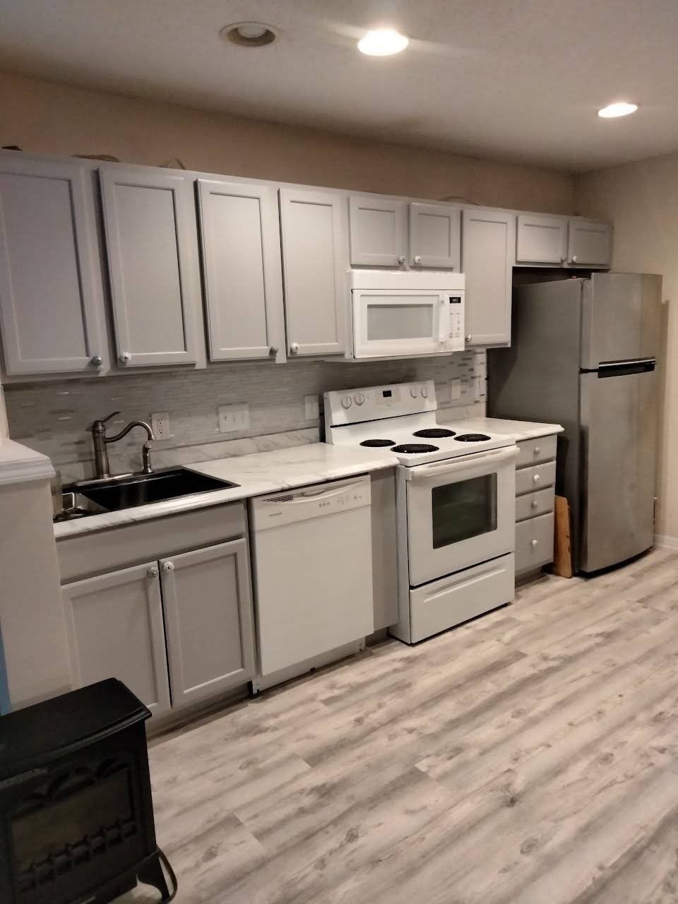 Kitchen with gray cabinets, white appliances, light countertops, and wood-look flooring.