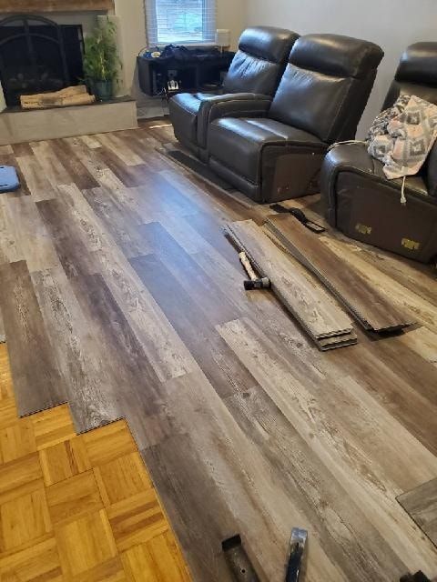 Installing new wood-look flooring over existing parquet. Brown recliner chairs and fireplace in the background.