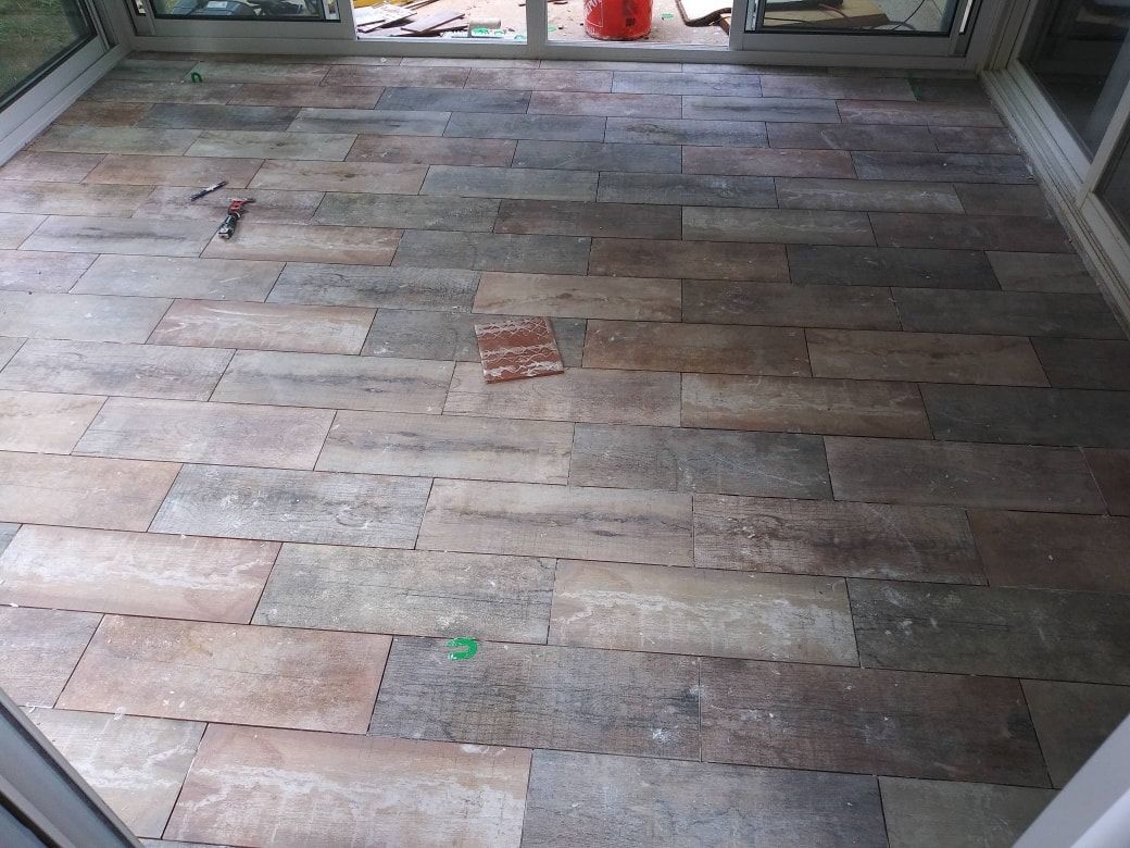Stone tile flooring in a sunroom, with gray, brown, and tan rectangles. Glass doors and windows frame the space.
