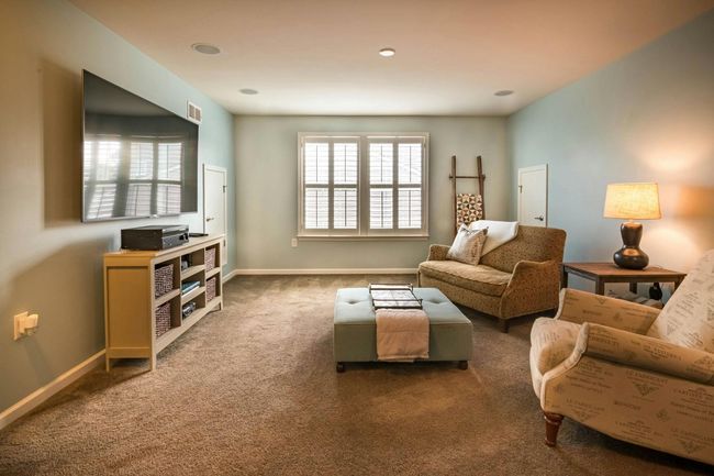 Living room with a large TV, two armchairs, a sofa, and a coffee table on a carpet.