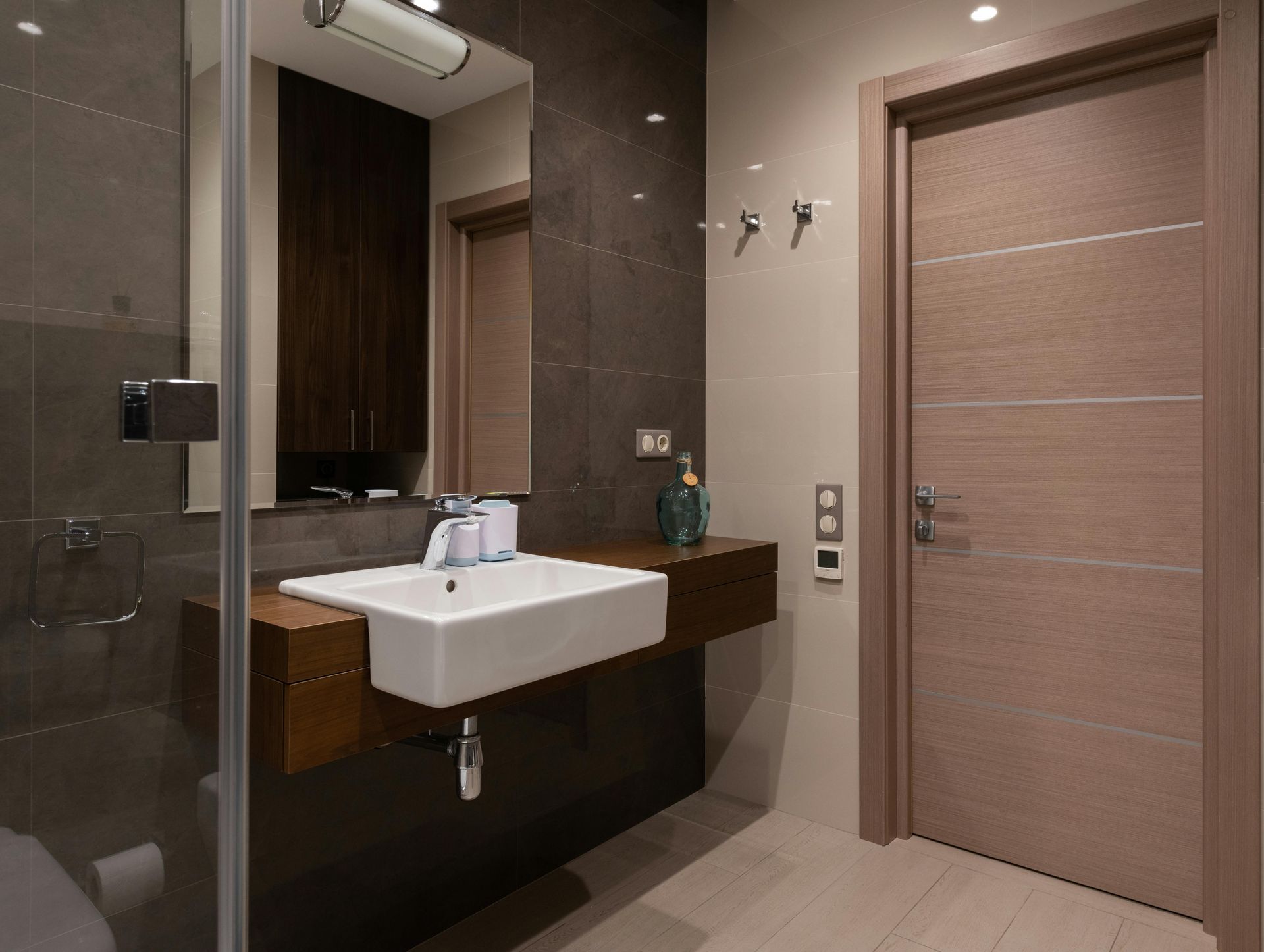 Modern bathroom with brown vanity, white sink, and light wood door.