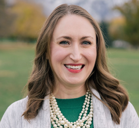 Headshot of Amanda Swennes, woman smiling with blue eyes, brown hair just past shoulders, red lipstick, wearing a green top with a gray sweater and a mulit-strand pearl necklace.