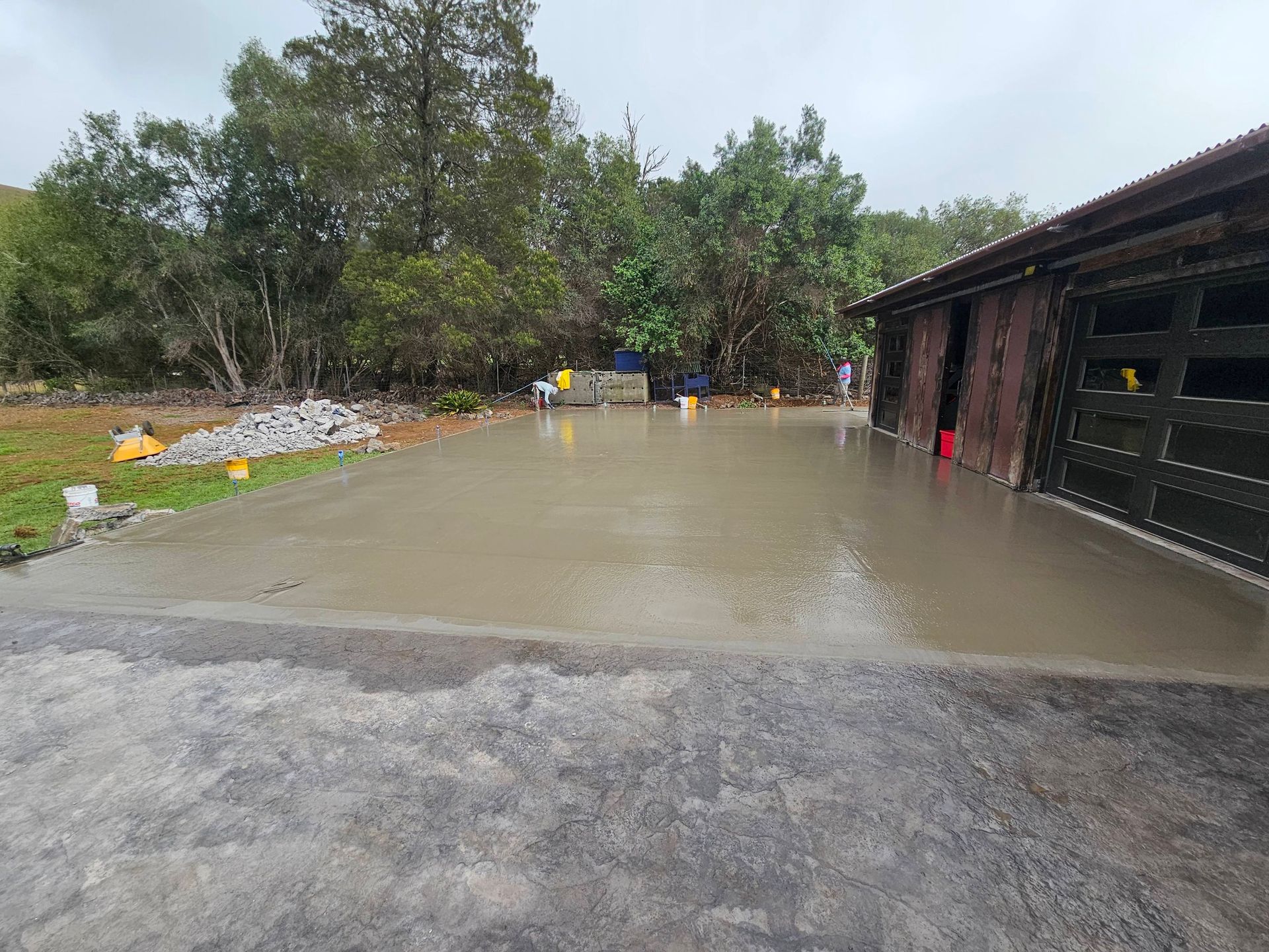 Flooded driveway beside a dark building and trees after heavy rain