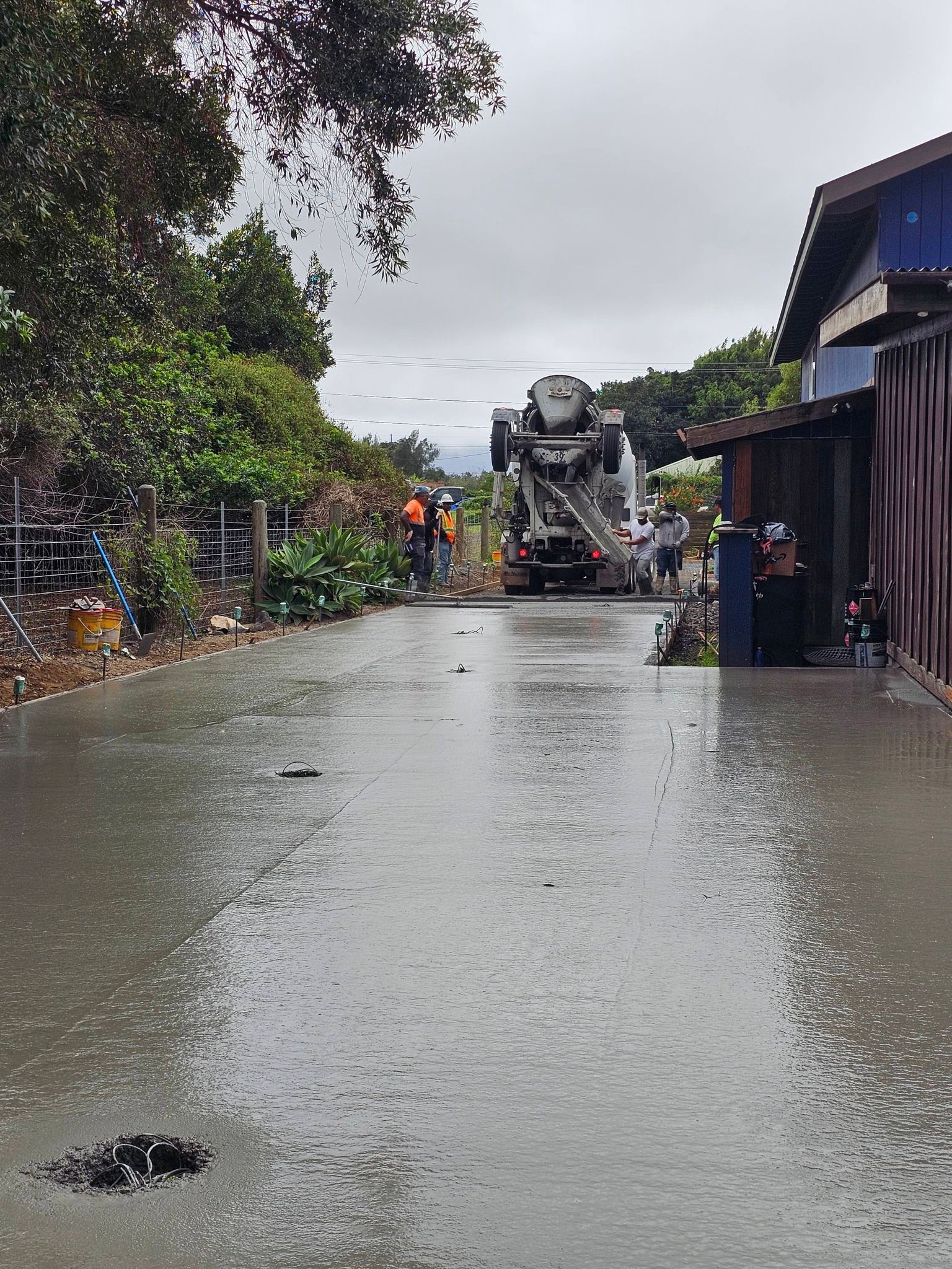 Flooded street with workers and a cement mixer truck near buildings and trees