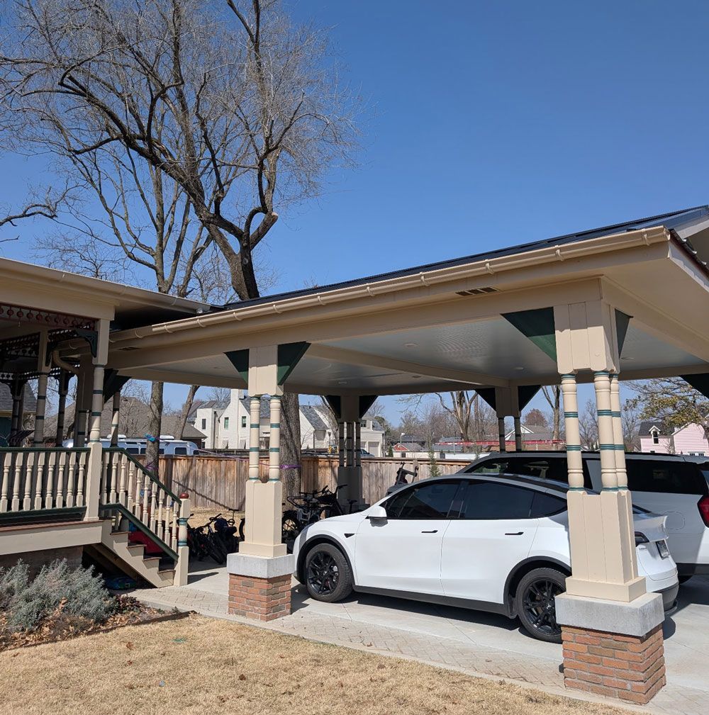 A white car is parked under a canopy in front of a house