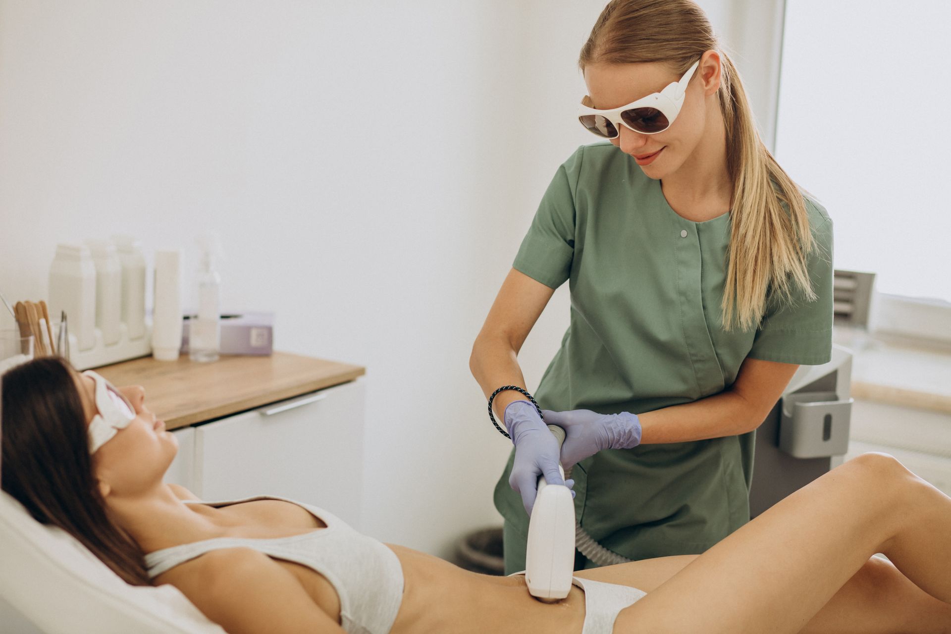 Woman in sunglasses receives a leg treatment from a clinician in a spa room