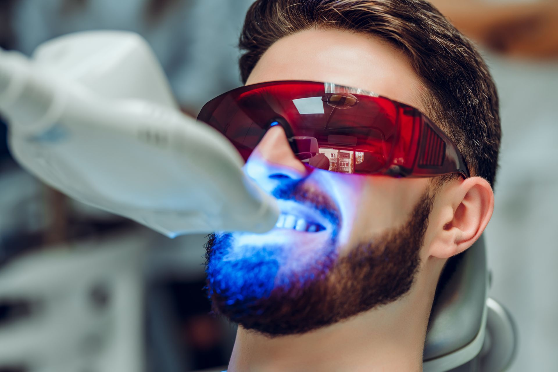 A man with a beard is getting his teeth whitened in a dental office.