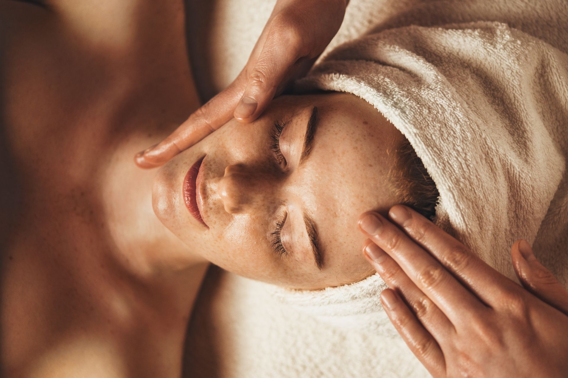 A woman with a towel wrapped around her head is getting a facial massage.
