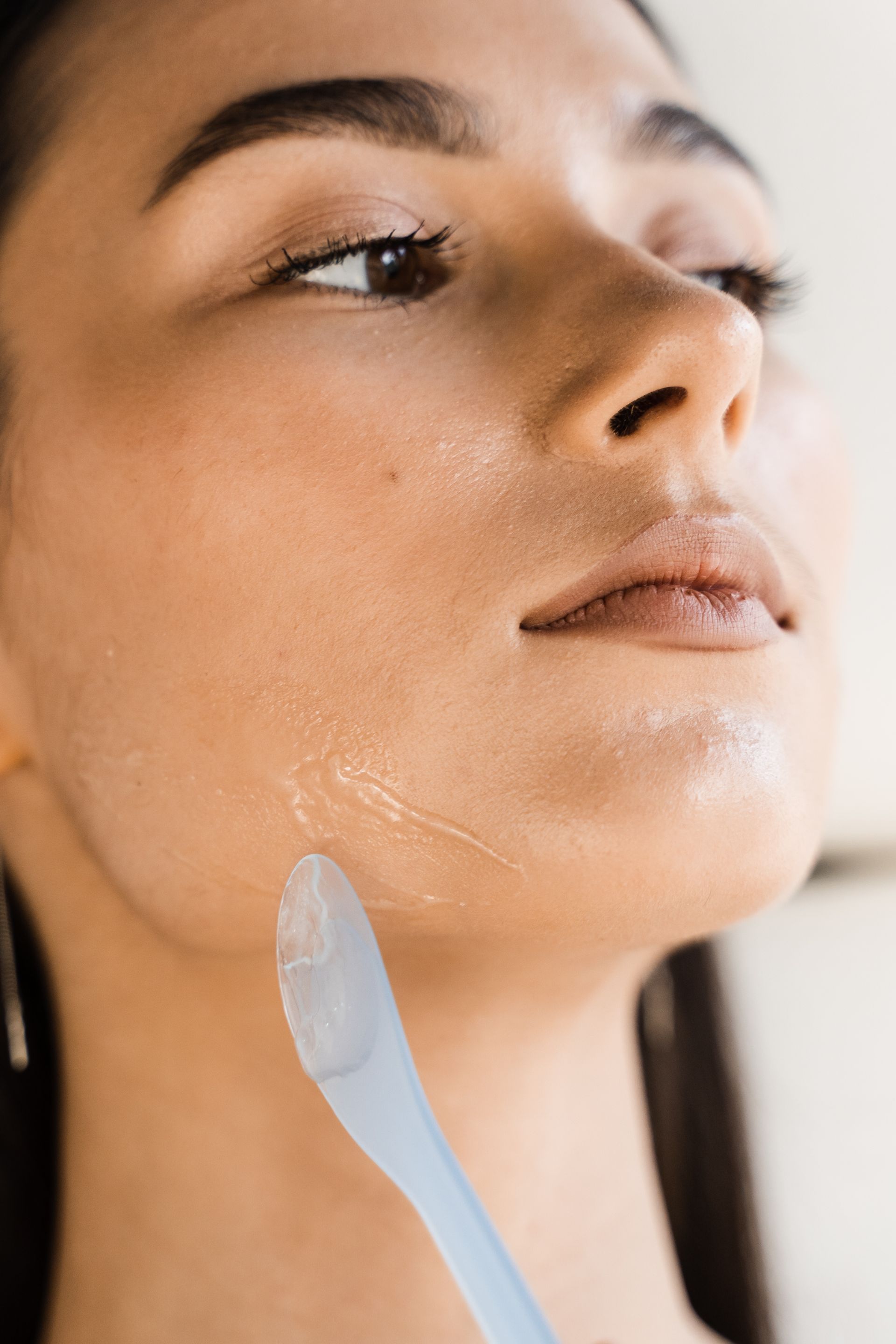 A woman is applying a cream to her face with a spoon.