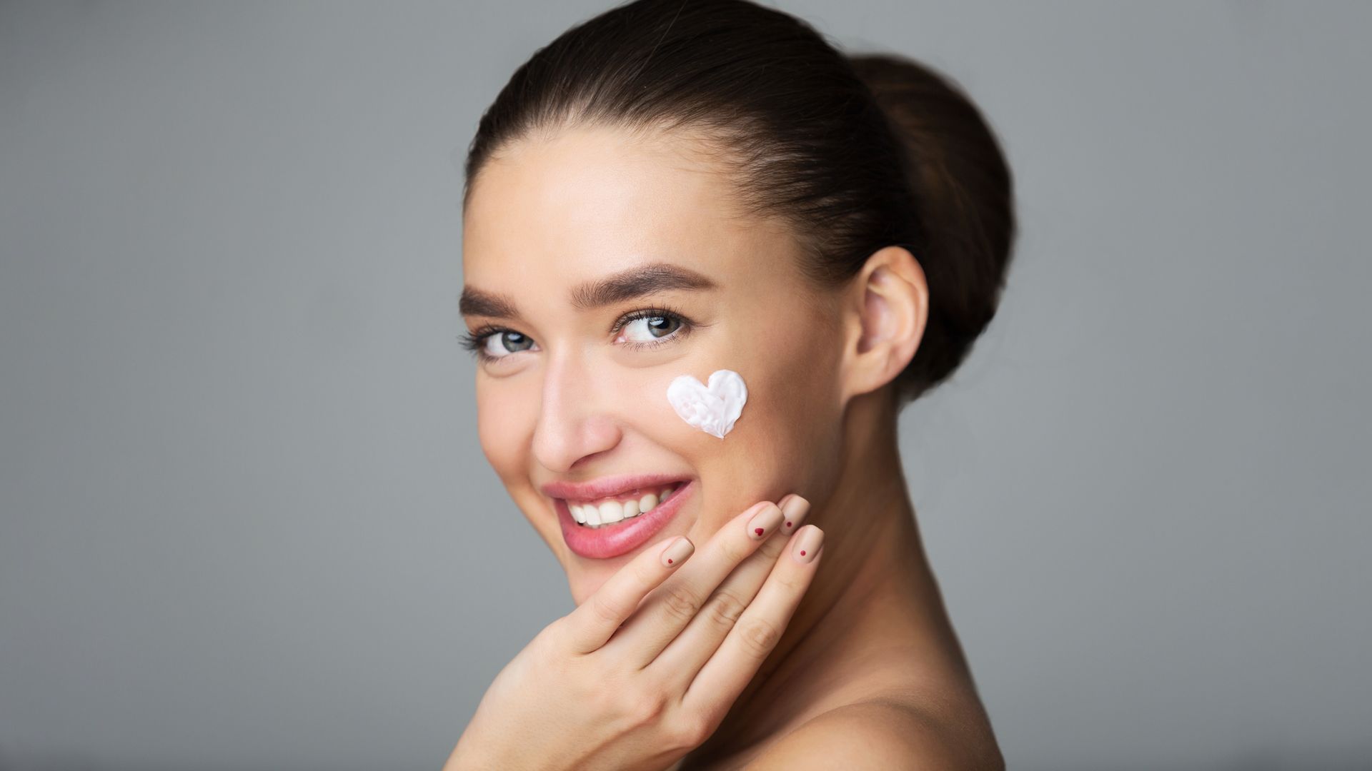 A woman is smiling and applying cream to her face.
