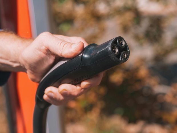 Hand holding a black EV charging connector, preparing to plug it in.