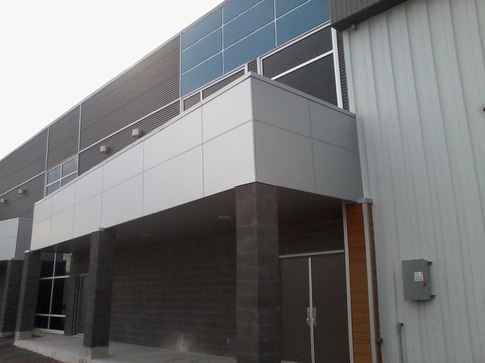 Façade de bâtiment moderne avec panneaux gris et blancs, entrée avec colonnes gris foncé.