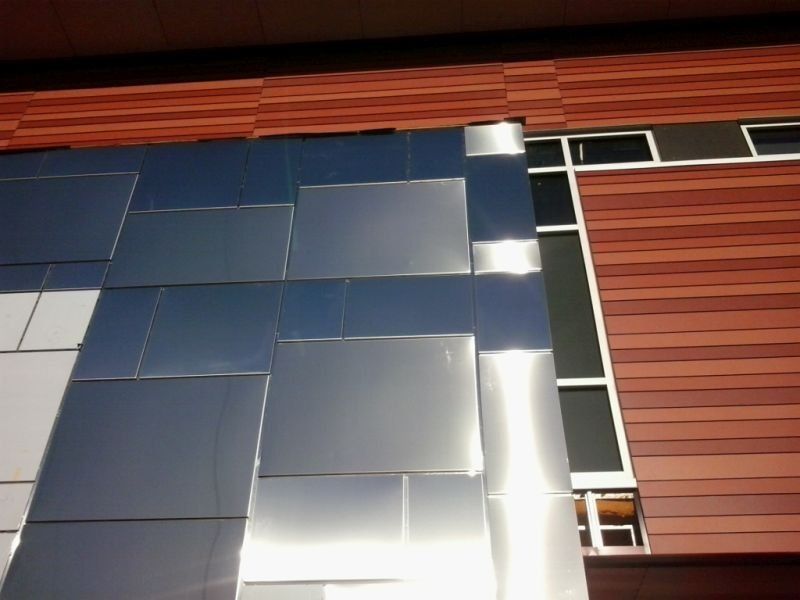 Façade moderne du bâtiment avec panneaux métalliques brillants et bardage en bois brun rougeâtre.