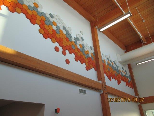 Fresque murale composée de carreaux hexagonaux orange, gris et blancs sur un mur blanc dans un bâtiment à poutres en bois.