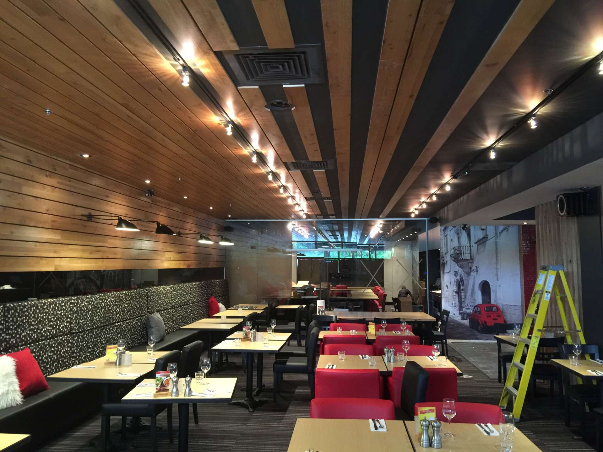 Intérieur du restaurant avec plafond en bois et noir, tables, banquettes rouges et échelle jaune.