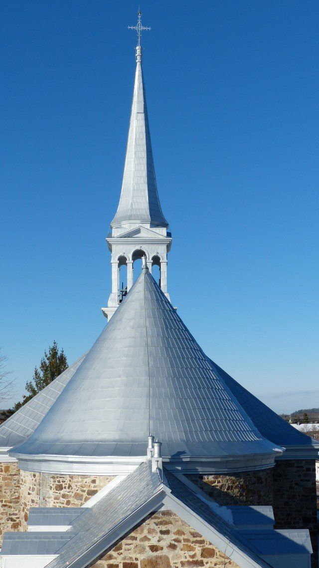 Un clocher d'église surmonté d'une croix, au-dessus d'un toit conique, se détachant sur un ciel bleu limpide.