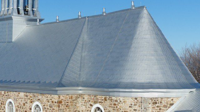 Toiture en métal argenté d'un bâtiment en pierre ornée de détails décoratifs pointus. Journée lumineuse et ensoleillée.