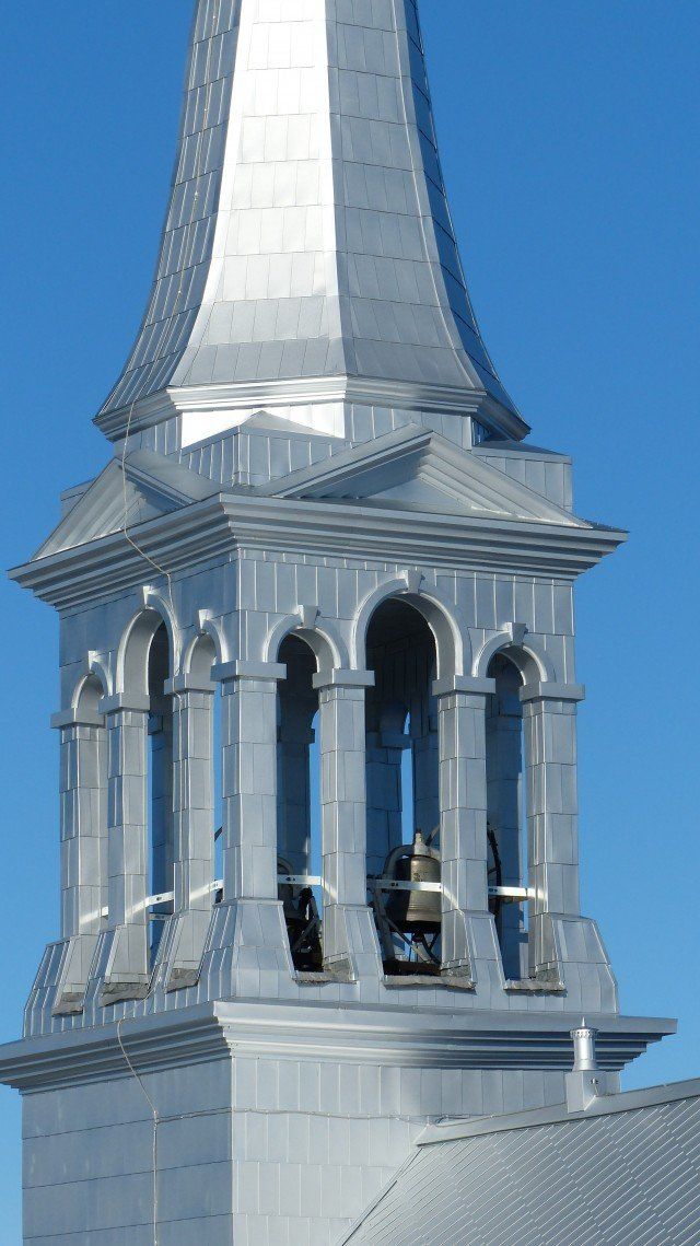 Clocher argenté d'une église se détachant sur un ciel bleu clair, laissant apparaître le clocher et la cime pointue.