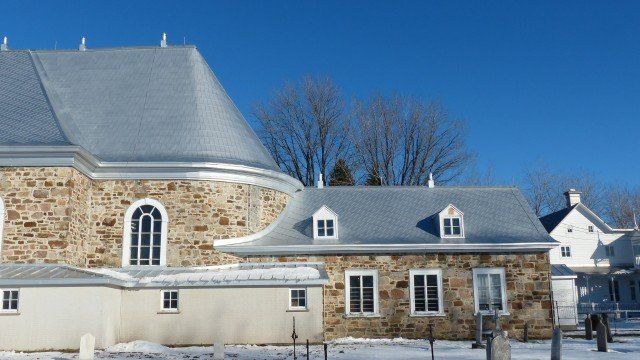 Des bâtiments en pierre aux toits gris se détachent sur un ciel bleu limpide par une journée de neige.