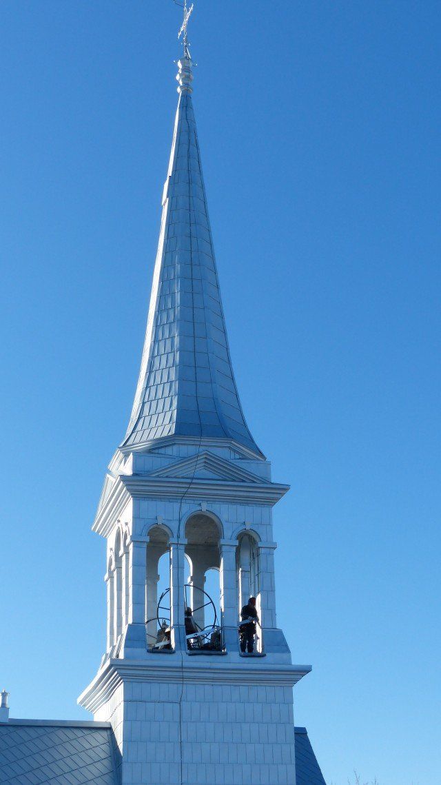 Clocher d'église blanc surmonté d'une croix, se détachant sur un ciel bleu clair.