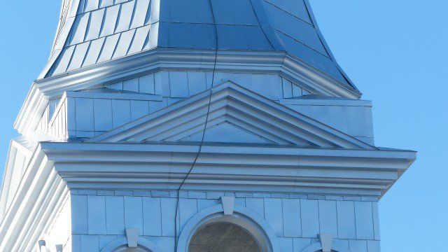 Clocher d'église blanc avec un fronton triangulaire et un toit pointu se détachant sur un ciel bleu clair.