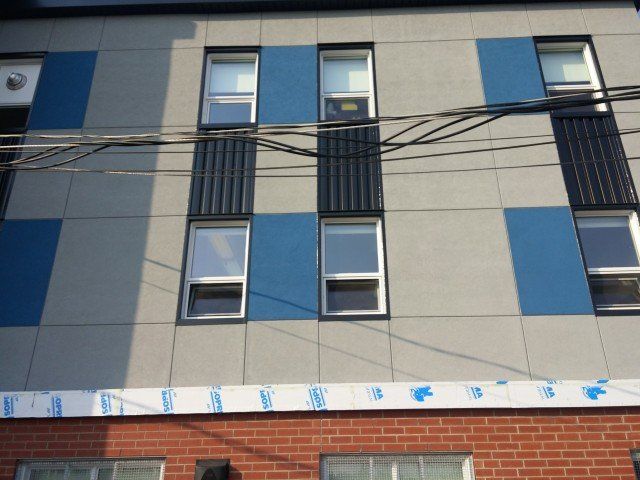 Façade du bâtiment avec panneaux bleus et gris, fenêtres et accents noirs, sur un socle en briques.