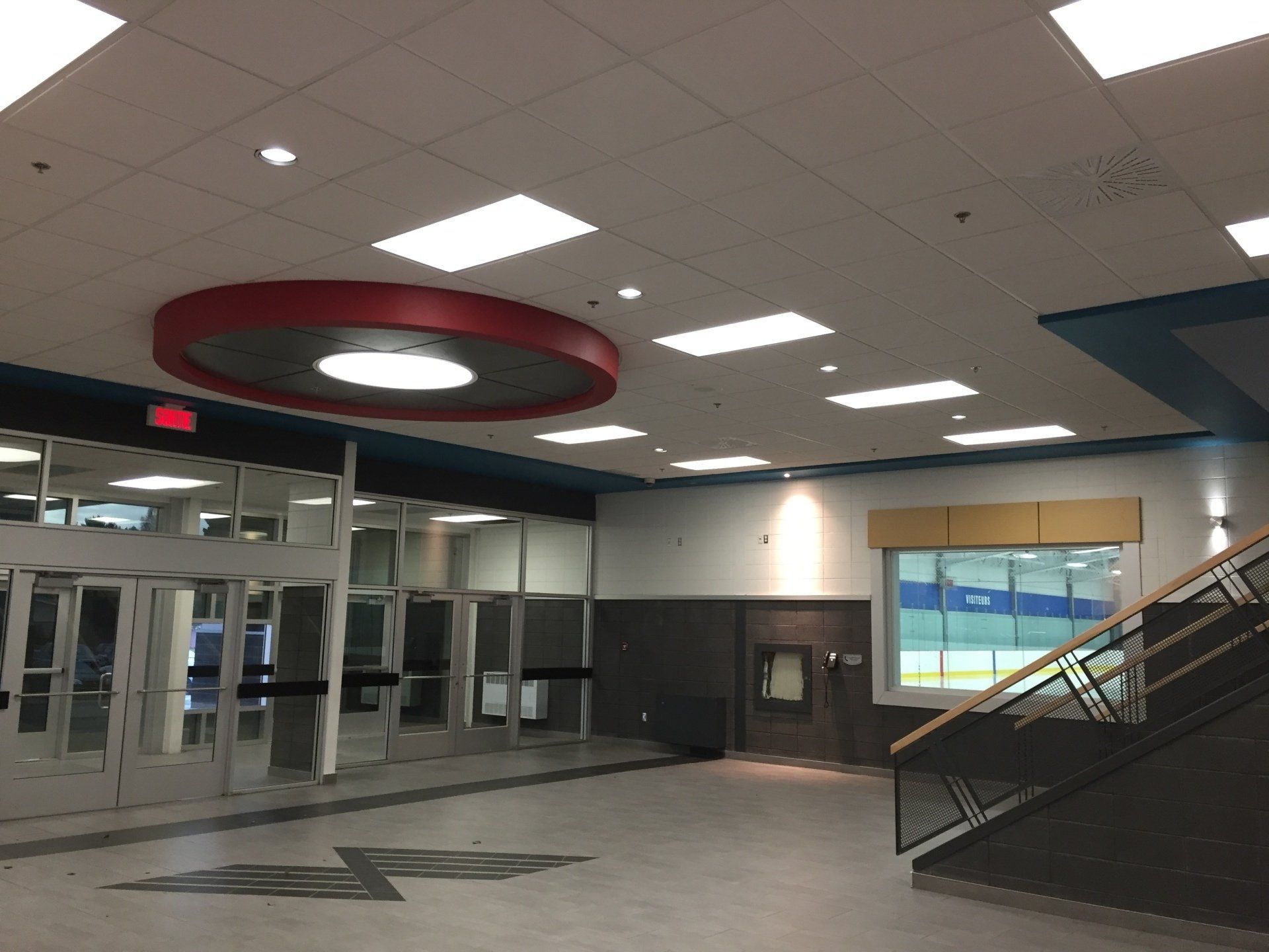 Intérieur d'une école avec portes d'entrée, luminaire circulaire rouge au plafond et escalier.