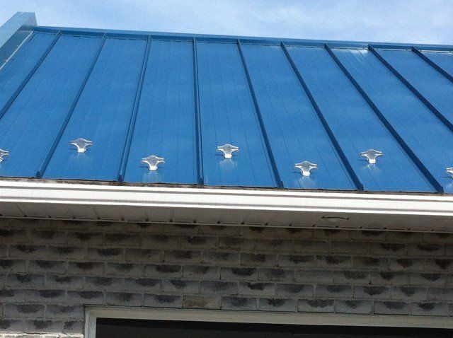Toiture métallique bleue avec éléments décoratifs transparents au-dessus d'un mur de briques et d'une gouttière.