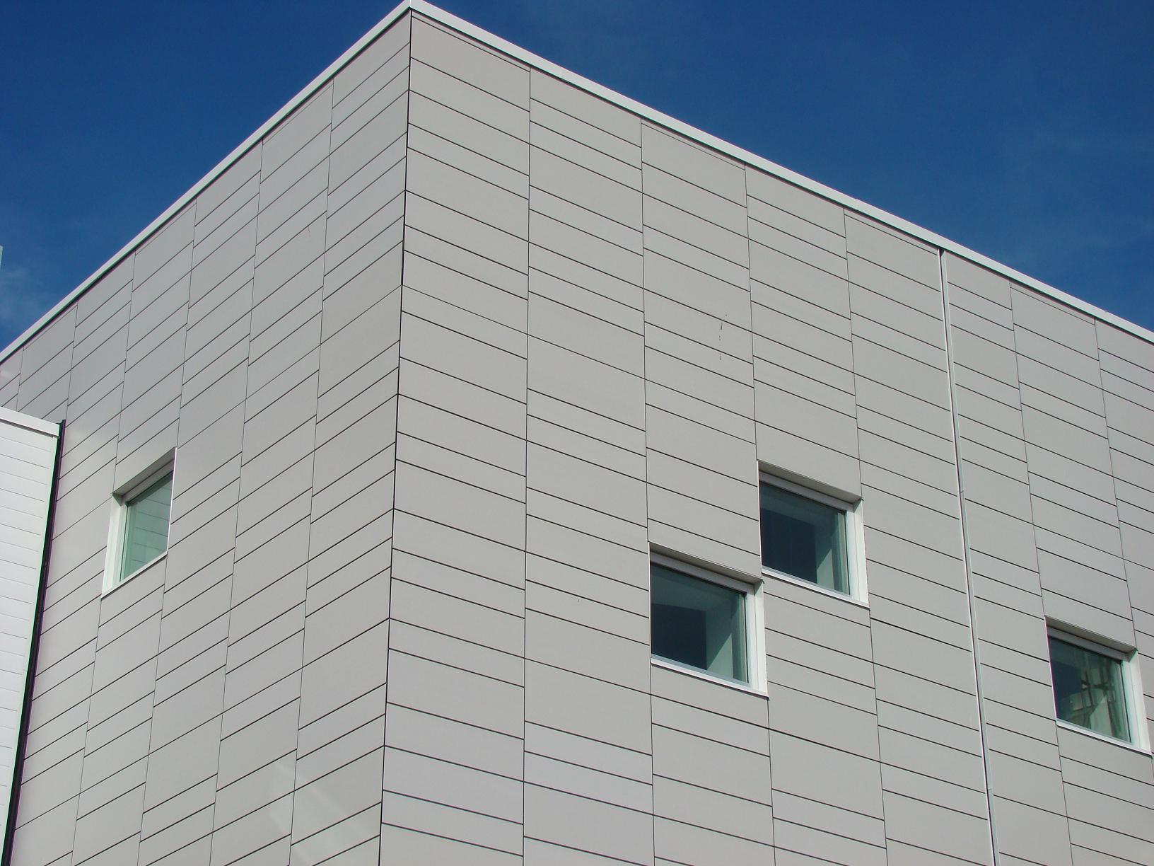 Bâtiment gris aux fenêtres carrées se détachant sur un ciel bleu.