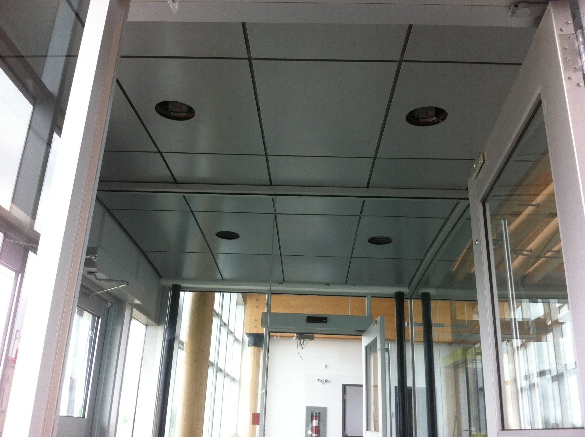 Plafond gris avec spots encastrés, au-dessus d'une porte à encadrement en verre et métal.