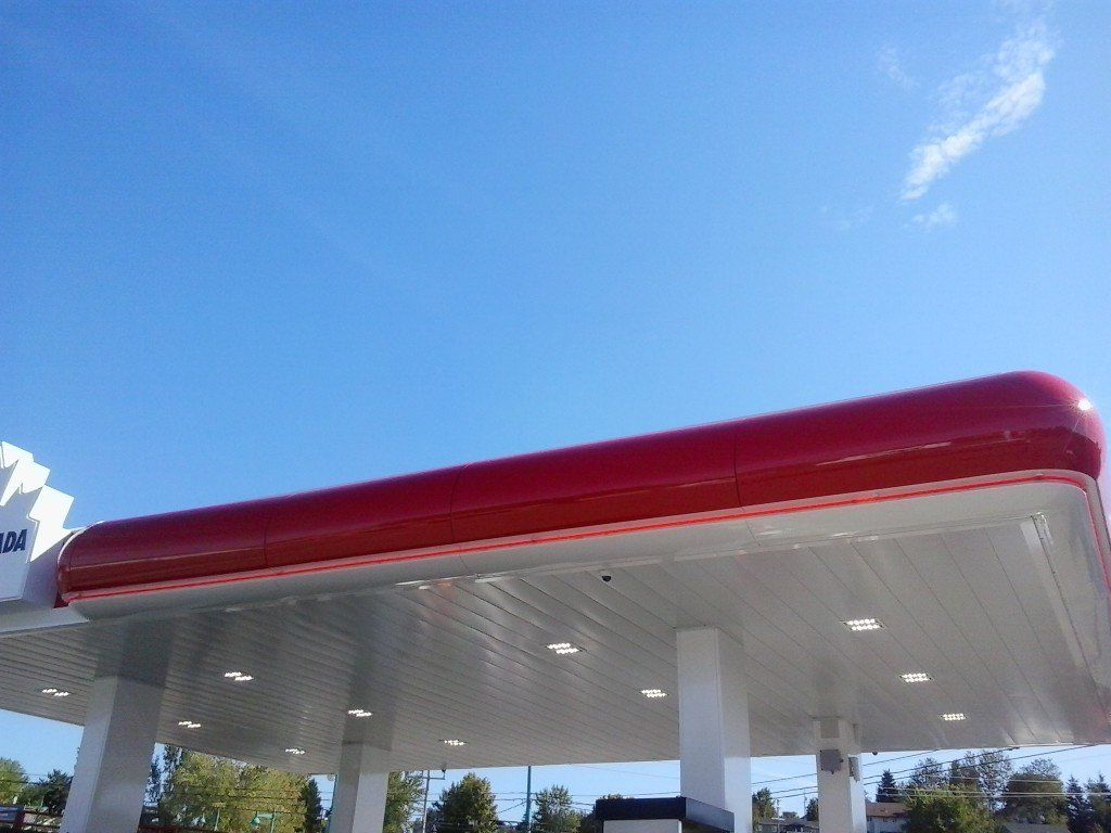 Auvent rouge et blanc d'une station-service sous un ciel bleu azur.