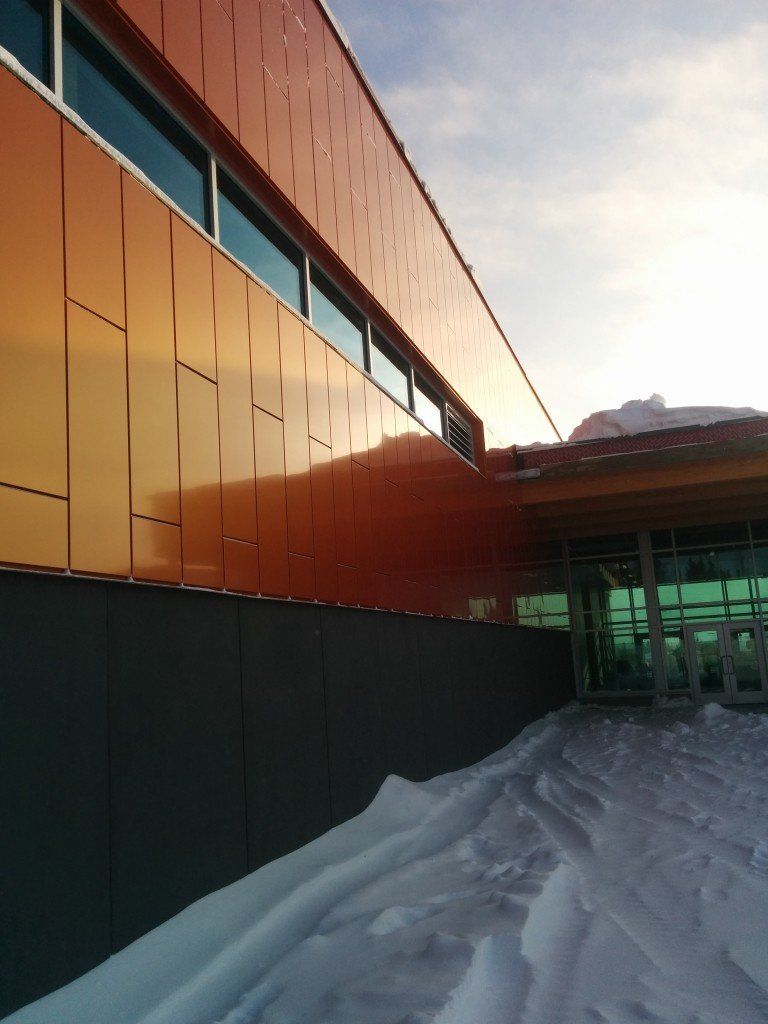 Façade d'un bâtiment orange et gris sous la neige, sous un ciel lumineux.