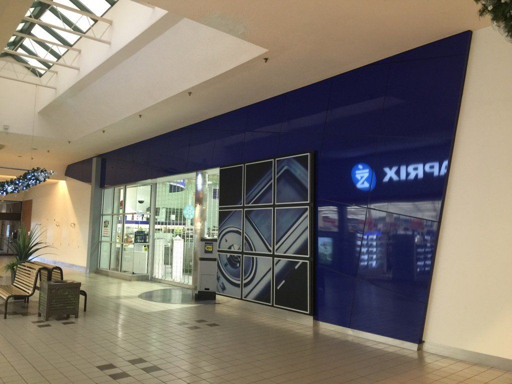 Façade bleue dans un centre commercial, avec vitrines exposant des marchandises. Un logo est visible.