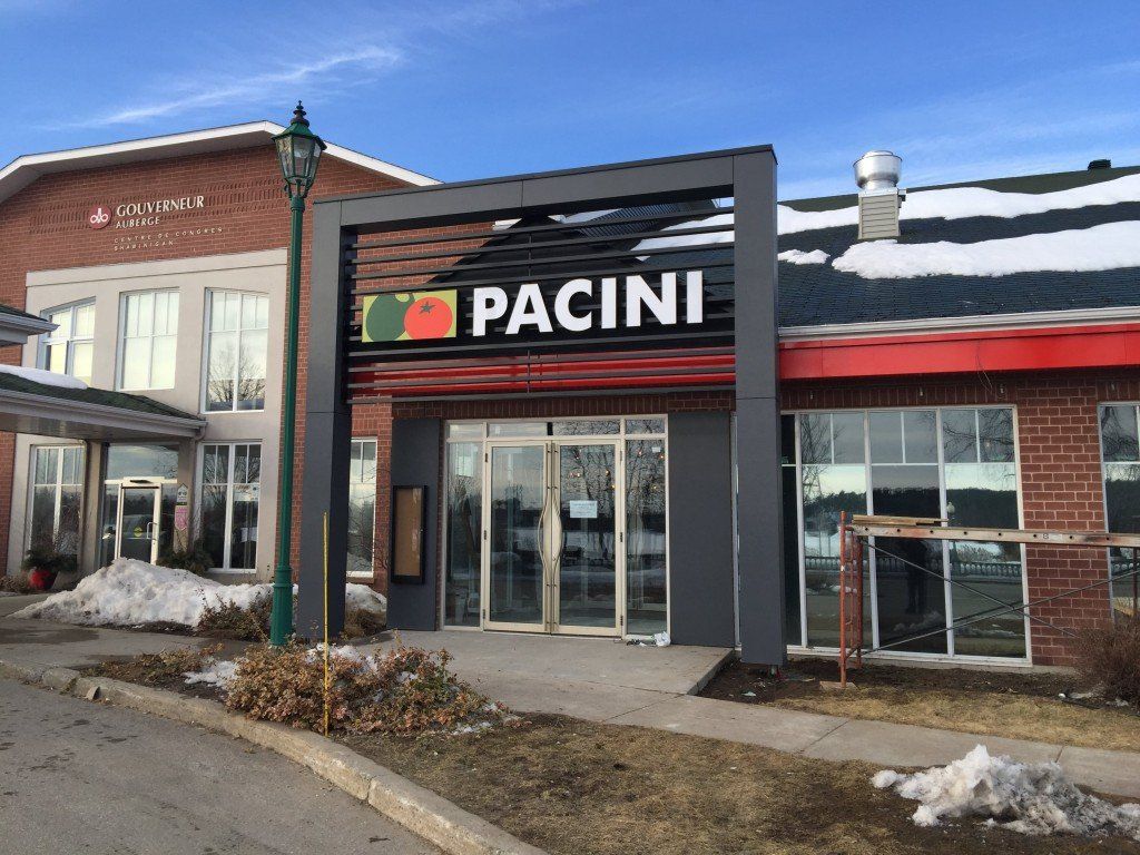 Entrée du restaurant Pacini, avec une grande enseigne devant un bâtiment en briques. Neige au sol.