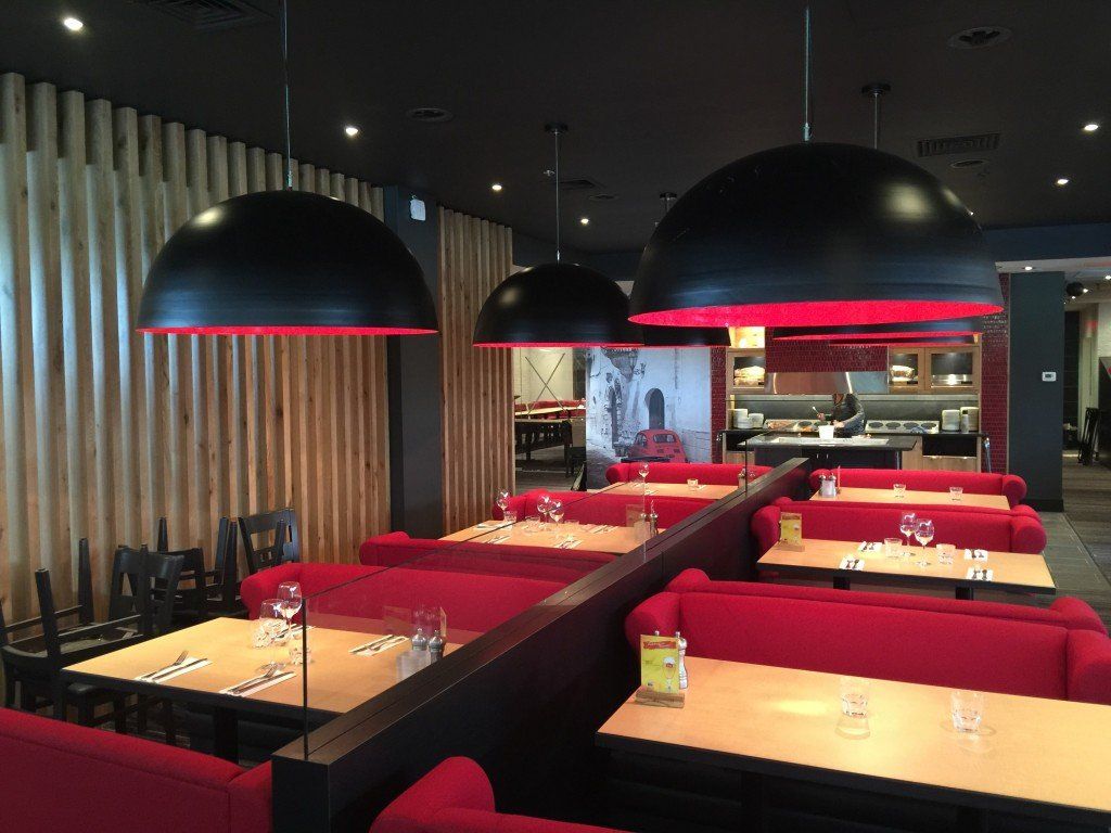 Intérieur de restaurant avec banquettes, tables et suspensions lumineuses en forme de dôme noir rehaussées de touches de rouge.