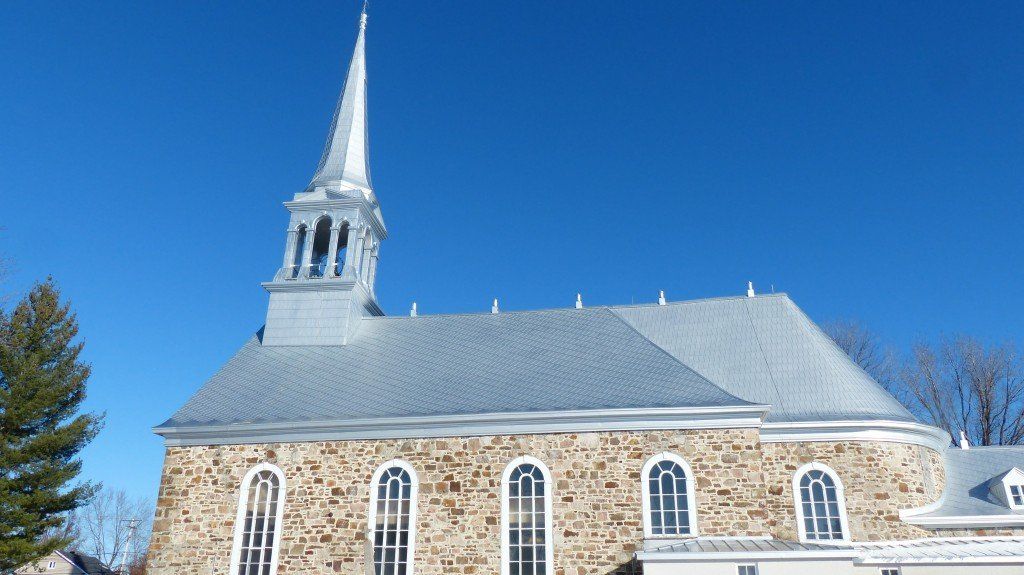 Église de pierre avec une flèche argentée se détachant sur un ciel bleu limpide.