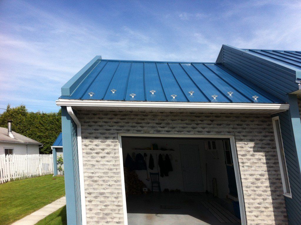 Toit en métal bleu sur un garage à façade en briques et ciel bleu.
