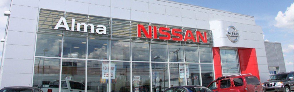 Concessionnaire Nissan à Alma, avec des vitrines, des touches de rouge et des voitures garées à l'extérieur.