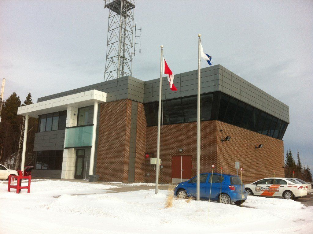 Un bâtiment orné de drapeaux, un sol enneigé, une tour de communication en arrière-plan et des voitures garées.